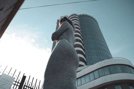 A girl with a beautiful figure in a gray dress near a tall building