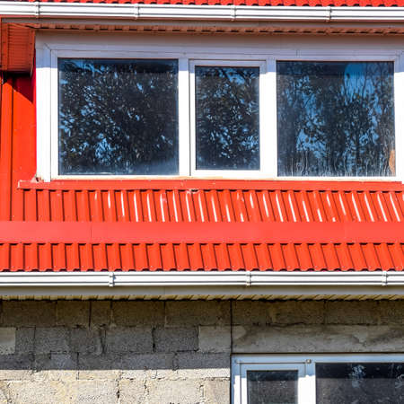 House with plastic windows and a red roof of corrugated sheet. Roofing of metal profile wavy shape...