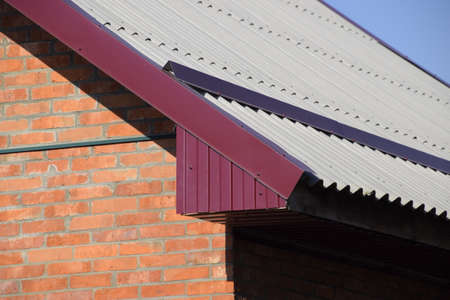 Corrugated metal profile of cherry color on the roof of the house. Corrugated metal profile of...