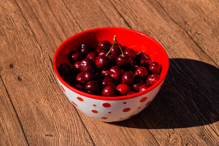 Berries of a sweet cherry on a wooden background in a plastic cup. Ripe red sweet cherry.
