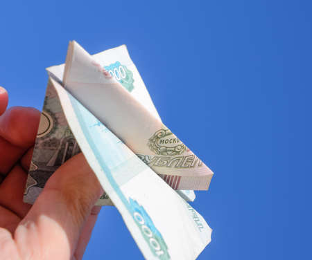 Denominations of Russian money, folded in the airplane against the blue sky in hand.