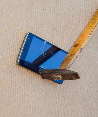 Hammer and smartphone. The screen of the smartphone, a broken hammer. The destruction of the phone.