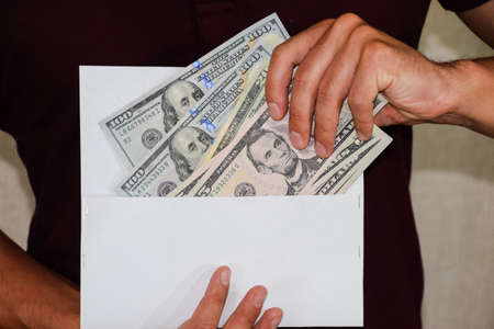 Money in a white envelope in the hands of a man. Dollars, a wad of dollars.の写真素材