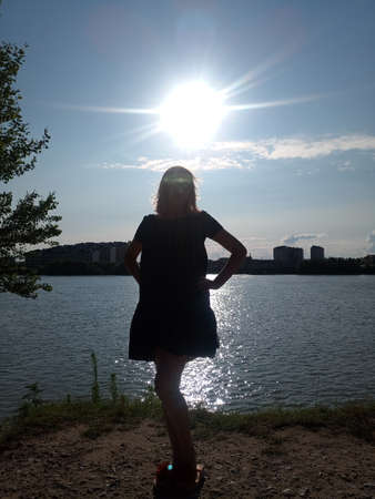 Silhouette of a girl against the background of a river in a backlight. The girl behind the sun by the river.の写真素材