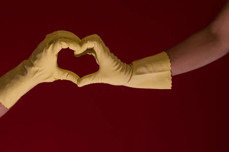 Hands with yellow gloves making a symbol of a heart on a red background. Photo with copy space. Love in time of coronavirusの写真素材