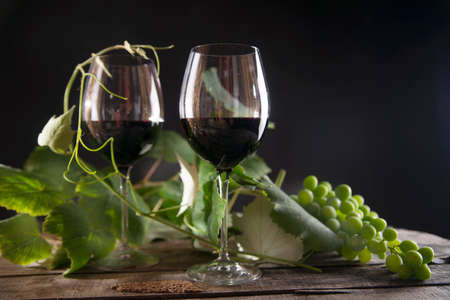 Glass of red wine with bottle and bunch of sour grapes on a black backgroundの写真素材