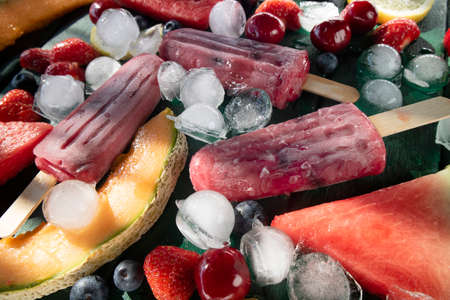 Photographic shot of popsicles made with red fruit on a table served with various fruitの写真素材
