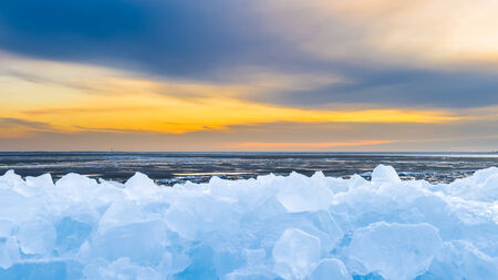 Early morning winter landscape with sunrise and drifting ice floats near costline in the Netherlandsの写真素材