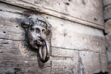Simpel old metal door handle knocker in head shape with wooden background