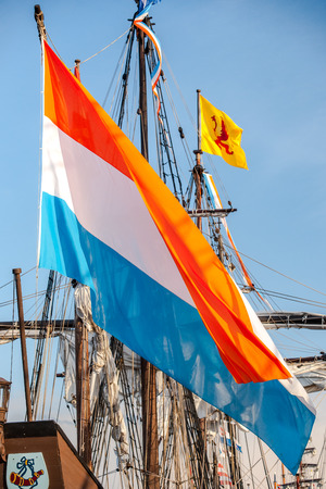 Colorful Dutch flag fluttering on cloudy day on the aft deck of a wooden historic dutch sailboatの写真素材