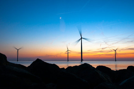 Romantic atmospheric sunset over the largest lake in the Netherlands (Ijsselmeer). Modern windmills stand in the water in a wind farm with a view from the dike and the basalt blocks of water protection.の写真素材