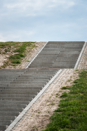 Stairway to heaven. Cultivated landscape with upward climbing stair stairs. Sea dike with green grass and cloudy clouds give way to the landscapeの写真素材