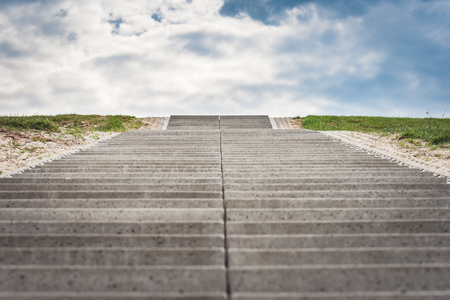 Stairway to heaven. Cultivated landscape with upward climbing stair stairs. Sea dike with green grass and cloudy clouds give way to the landscapeの写真素材