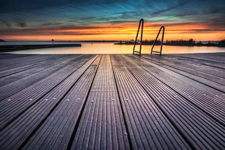 Outdoor swimming pool at the lake with metal aluminum swimming stairs with an impressive intense sunrise.の写真素材