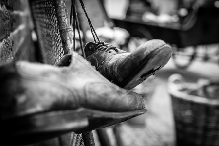 Worn brown leather shoes with holes in the soles, hanging on old vintage fence with the laces tiedの写真素材