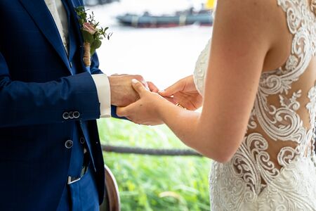 Fingers of the bride slide the gold wedding ring on the hand of the groomの写真素材