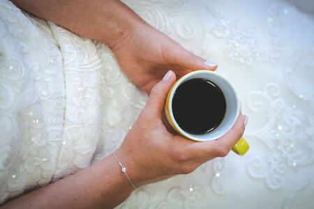 Bride hold coffee cup in the hands
 fixed above wedding dress with white and lace finish at weddingdayの写真素材