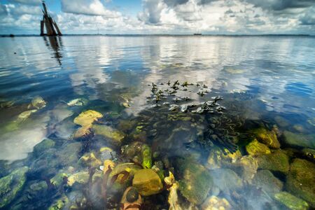 Beautiful moving cloudy sky with white clouds and blue sky above a rocky lake with clear water,...