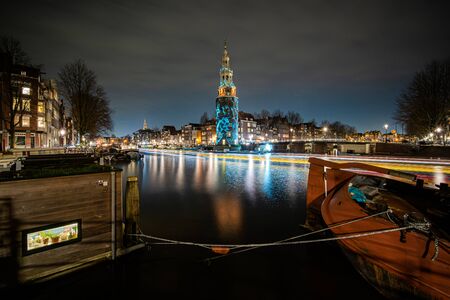 Amsterdam, Netherlands - December 29, 2019 : artfully lit tower with light project and passing boats at nightの写真素材