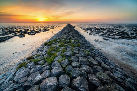 Mud flat of the 'waddenzee' during low tide under scenic dramatic sunset sky with clouds