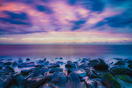 Gentle sunset on the sea coast. Stunning view of waves crashing on rock formations under pastel skies at West Kapelle, Zeeland, Netherlandsの写真素材