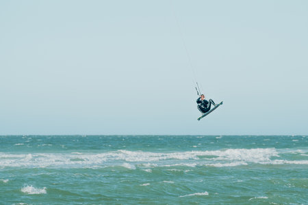 People enjoy riding kite surf board in sun uv protection suit on bright sunny day at sea or ocean shore kitesurfing camp spot. Water sports adrenaline fun adventure activityの写真素材