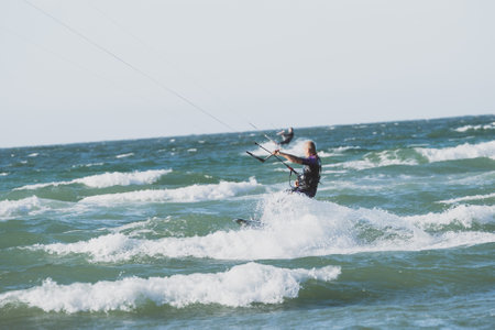People enjoy riding kite surf board in sun uv protection suit on bright sunny day at sea or ocean shore kitesurfing camp spot. Water sports adrenaline fun adventure activityの写真素材