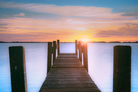 Water and lake with wooden jetty (pier) with the setting sun on the horizon and a cloudscape sky in beautiful colors. Countryside landscapes of Netherlands, Giethoornの写真素材