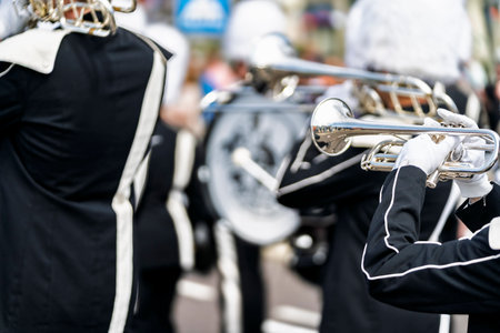 Musician in a black and white uniform plays a silver trumpet, part of a marching band performance...