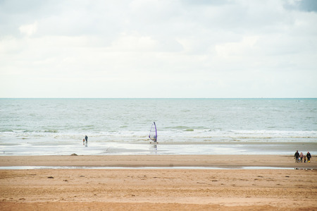 Surfing on the beach in front of waves at autumn with some people walking byの写真素材