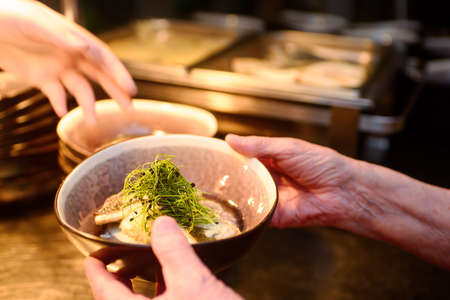 Hand with a bowl containg fish and fresh cuckooflower and blurred buffet in the backgroundの写真素材