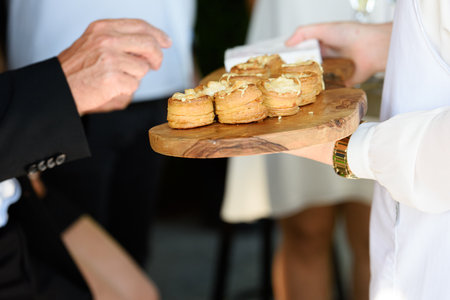 hand taking appetizer with a cheese filling on a wooden plate hold by a waiter in a white vestの写真素材