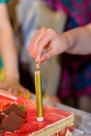 closeup of a womans hand starting with a match a fountain firework on a cakeの写真素材
