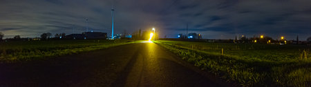 A serene nightscape of illuminated windmills standing tall in a vast panoramic field, surrounded by...