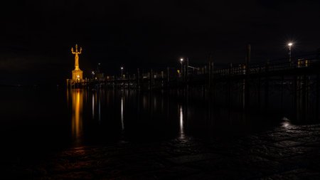 Golden statue of Imperia illuminated at night, standing on a platform at the edge of Lake Constance, Germany.の写真素材