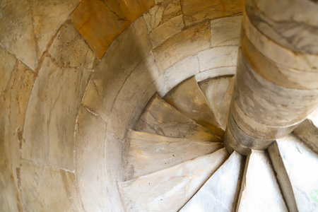 Spiral staircase crafted from stone, featuring tightly packed steps coiling around a central column. The stone surfaces are smooth with varied light and dark tones.の写真素材