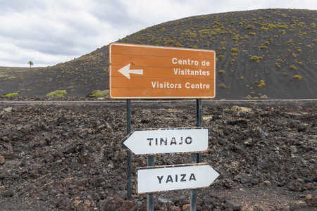Signpost located on a rugged volcanic landscape in Lanzarote, Canary Islands, Spain. The sign is mounted on a metal pole and consists of three directional panels.の写真素材