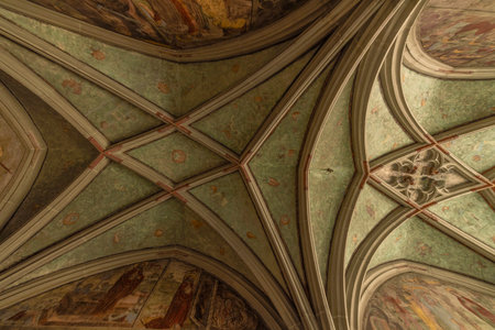 The image showcases the vaulted ceiling of a Gothic church, featuring intricate ribbed vaults with diagonal ribs crossing at the center. The ceiling is adorned with faded frescoes.の写真素材