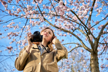 redhead girl taking photos in front of cherry blossomの写真素材