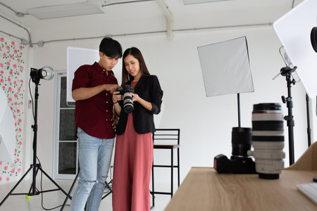 An Asian model is checking the photo on the camera, with an Asian photographer standing beside her. With both smiling faces With a front camera film and lens camera placed on a comの写真素材