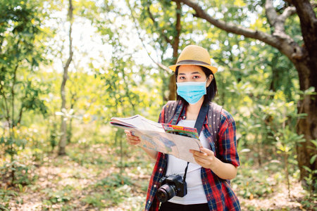 Asian woman traveler wearing face mask and holding map in the forest.の写真素材