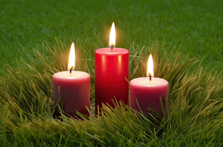 Three red candles on green grass, close-up, horizontal pictureの素材