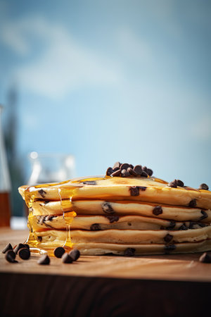 Stack of pancakes with chocolate chips and honey on a wooden table.の素材