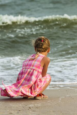 Sad little girl child sitting on the beach near the seaの写真素材