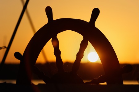 Ship's wheel on sunset backgroundの写真素材