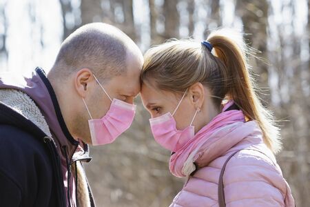Man and woman in medical masks touch each others heads in nature during quarantine.
