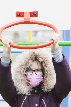 Portrait of a girl in a medical mask and glasses at the playground.
