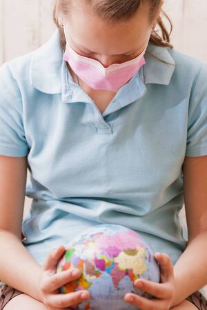 Girl in a medical mask touches the globe with her hands.の写真素材