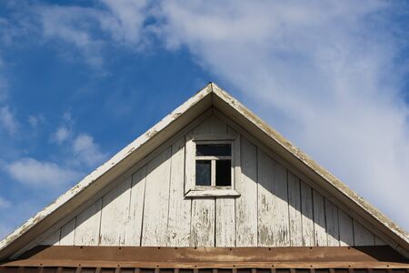 The roof of an old wooden house with a window against the skyの写真素材