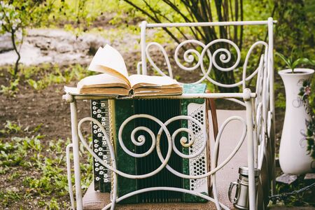 Accordion with an open book in the wind in the garden on an old vintage bedの写真素材